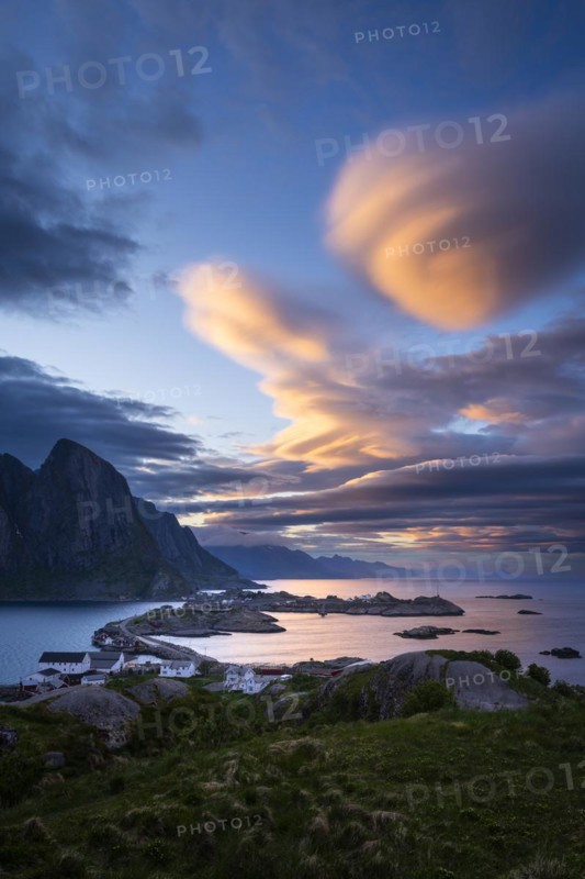 Cloudy landscape. The villages of Olenilsoy, Toppoya (Toppoy) and Hamnoy as well as the mountain Festhaeltinden. View over the sea towards Flakstadoya and Vestvagoya. Several coloured lenticular clouds (lenticularis) in the blue sky. At night at the time of the midnight sun. Early summer. Moskenesoya, Lofoten, Norway, Europe