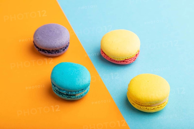 Yellow, purple and blue macaroons on blue and orange pastel background. side view, close up. Minimalism, morning, contrast concept