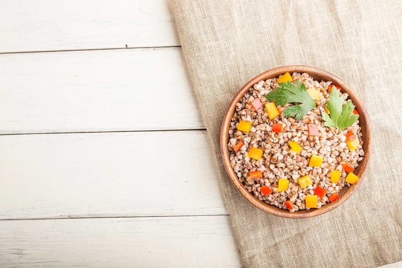 Buckwheat porridge with vegetables in wooden bowl on a white wooden background and linen textile. Top view, flat lay, copy space. Russian traditional cuisine