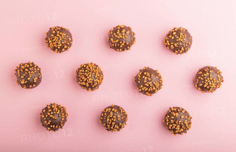 Chocolate caramel ball candies with almonds in a row on a pastel pink background. top view, flat lay