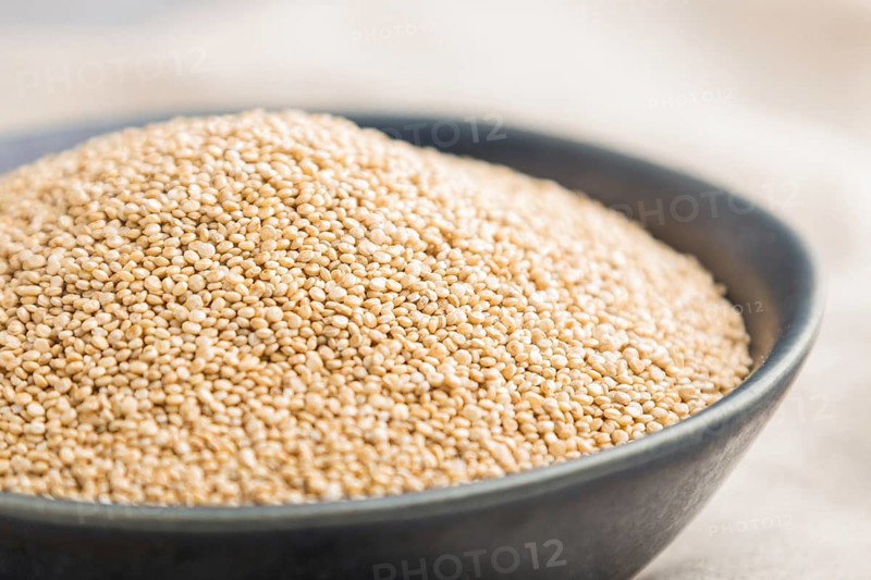 Blue ceramic bowl with raw white quinoa seeds on a gray concrete background and linen textile. Side view, close up, selective focus