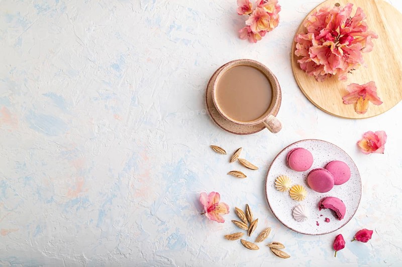 Purple macarons or macaroons cakes with cup of coffee on a white concrete background decorated with flowers. Top view, flat lay, copy space