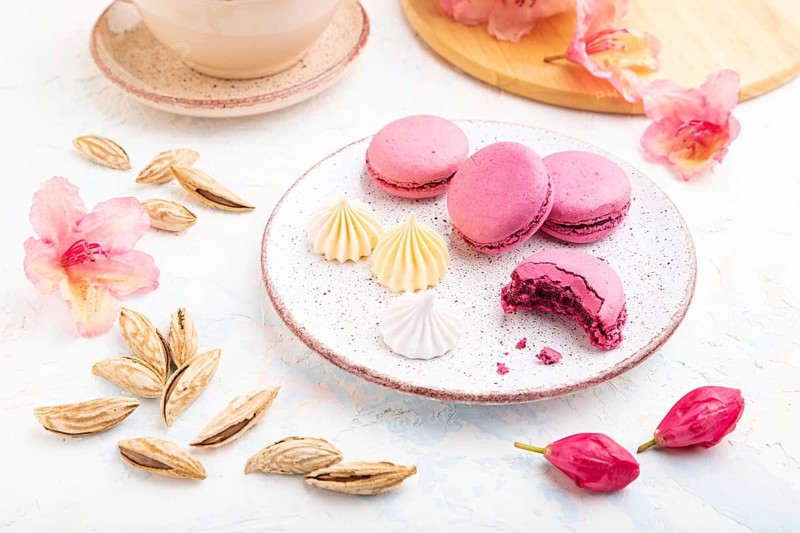 Purple macarons or macaroons cakes with cup of coffee on a white concrete background decorated with flowers. Side view, close up