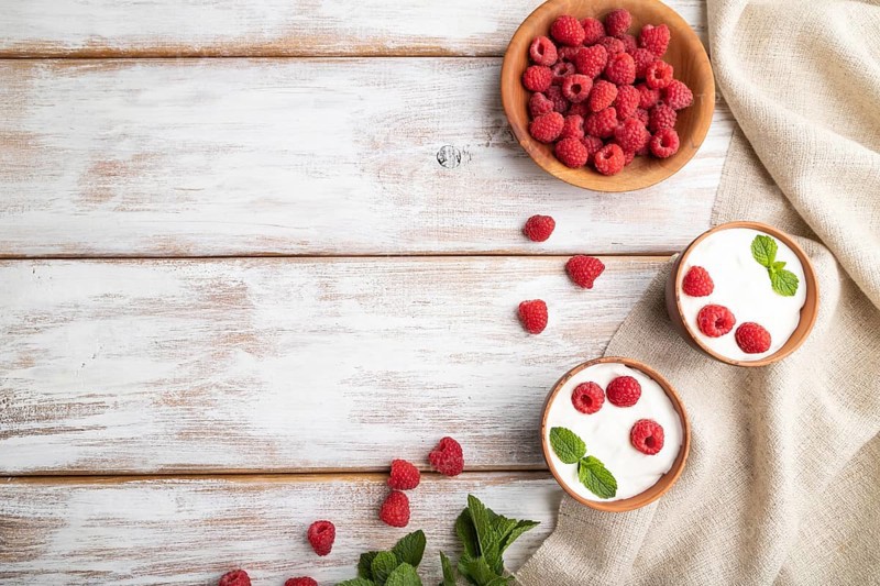 Yogurt with raspberry in clay cups on white wooden background and linen textile. top view, flat lay, copy space
