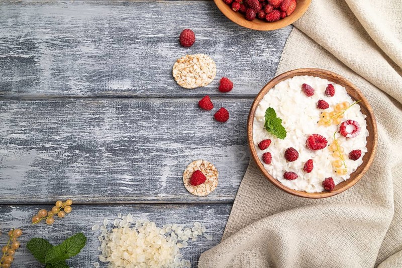 Rice flakes porridge with milk and strawberry in wooden bowl on gray wooden background and linen textile. Top view, flat lay, copy space