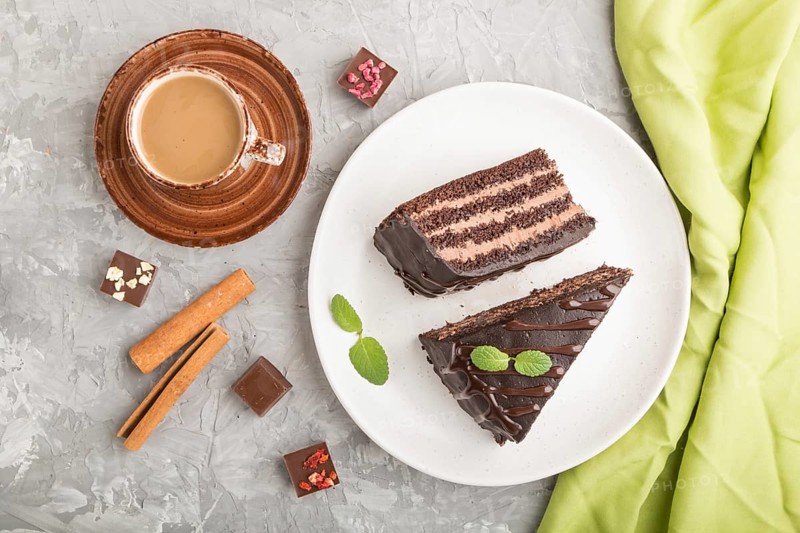 Homemade chocolate cake with milk cream and a cup of coffee on a gray concrete background with green textile. top view, flat lay, close up