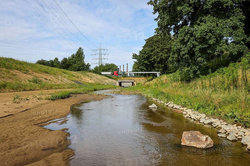 Bottrop, North Rhine-Westphalia, Germany, Renaturalised Boye, the tributary of the Emscher, was transformed into a near-natural watercourse, flood protection through newly designed flooding areas, the Boye is now free of wastewater after the construction of a parallel sewer, is part of the Emscher river system and thus part of the Emscher conversion, was previously an open, above-ground wastewater canal, mixed water canal with surface water and wastewater. At the back, car traffic on the B224 federal road bridge in front of the Prosper coking plant, ArcelorMittal Bottrop, Europe