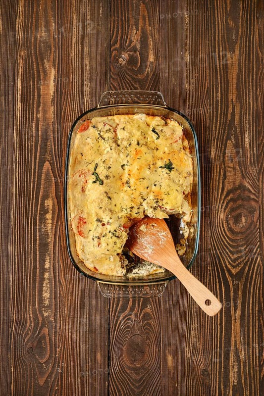 A casserole filled with cannelloni pasta, vegetables and herbs in a glass dish. A wooden spatula rests inside, ready to serve this comforting meal perfect for gatherings