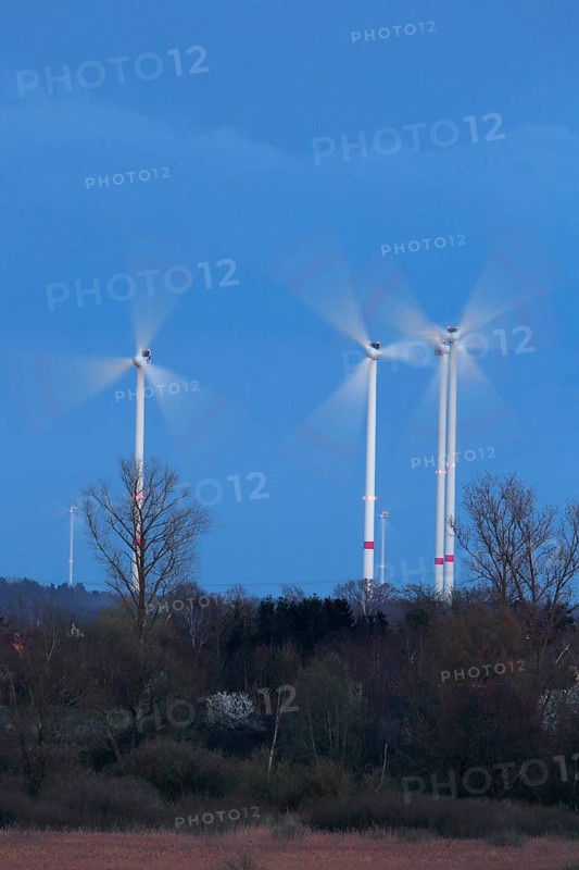 Luminous wind turbines rotating in an area surrounded by trees in the evening light, Wind turbines in the evening light, long exposure, Naturpark Flusslandschaft Peenetal, Mecklenburg-Vorpommern, Germany, Europe