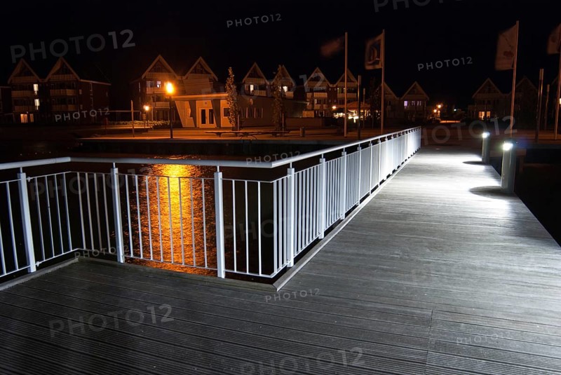 Pier with illuminated lamps, railings and light reflections in the water at night, flags and houses in the background, harbour village Müritz, Rechlin, Mecklenburg-Vorpommern, Germany, Europe
