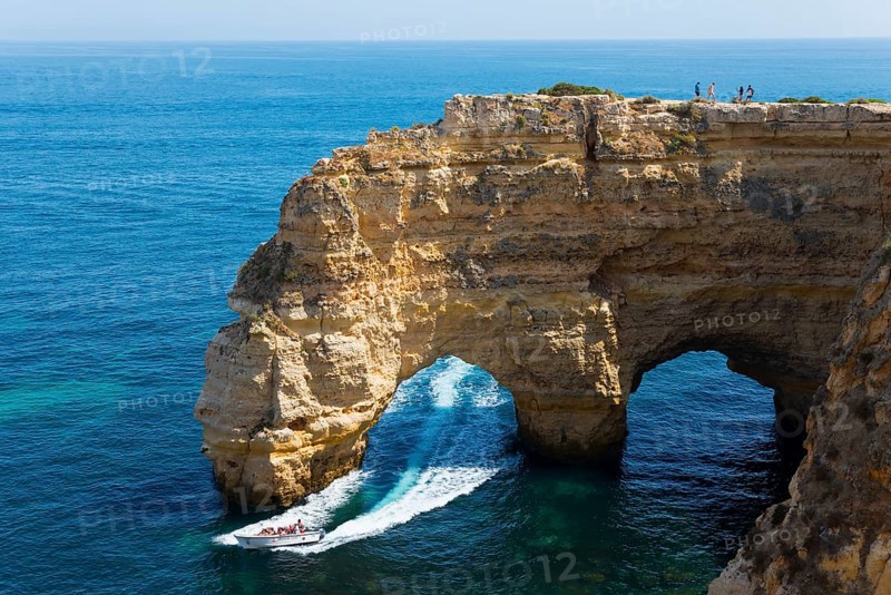 A boat sails under a natural rock arch along an impressive rocky coast, Praia da Marinha, double rock arch, Lagoa, Rocky Algarve, Algarve, Portugal, Europe