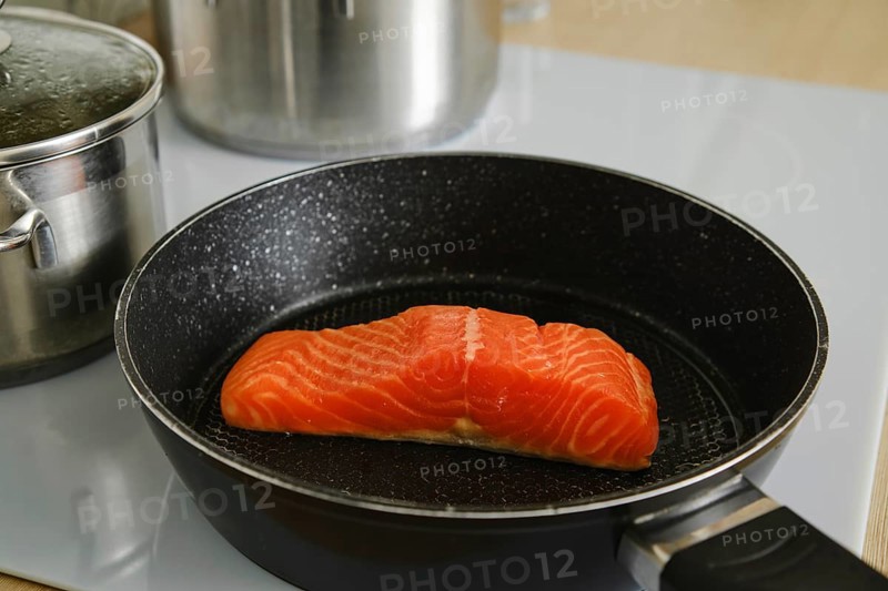 Closeup view of piece of fresh trout steak in a frying pan on electric stove