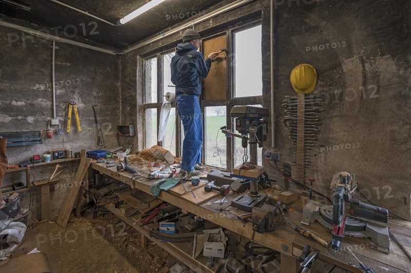 Young man in his workshop, standing on the workbench and repairing a window, Mecklenburg-Vorpommern, Germany, Europe