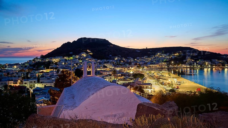 Agia Paraskevi Chapel, Illuminated coastal town at night with a view of the sea and hills in the background under a blue sky, Skala, Patmos, Dodecanese, Greek Islands, Greece, Europe