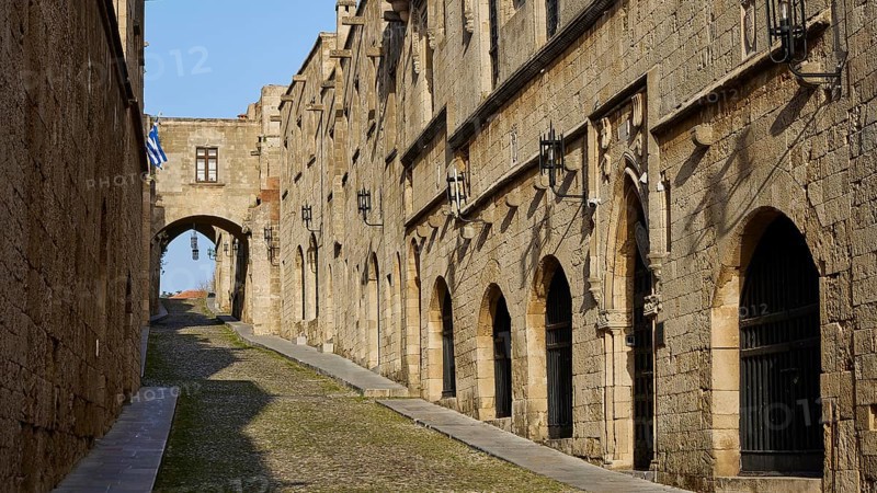 A historic alleyway with stone buildings and arches, blue and white flags in the background, Knights' Street, Rhodes Old Town, Rhodes Town, Rhodes, Dodecanese, Greek Islands, Greece, Europe