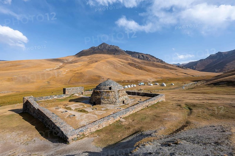 Historic caravanserai Tash Rabat from the 15th century, traditional yurts in the back between golden hills, Naryn region, Kyrgyzstan, Asia