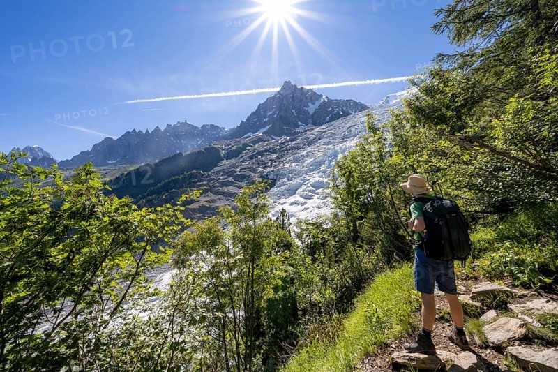 Hiker on hiking trail La Jonction, view of glacier Glacier des Bossons with sun star, behind summit of Aiguille du Midi, Chamonix, Haute-Savoie, France, Europe