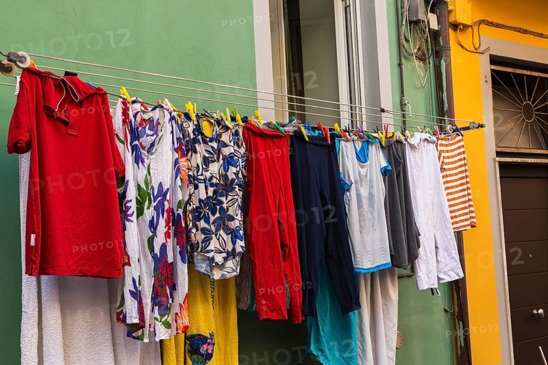 Men's and women's washed clothes drying on clothesline of green painted with white trim stucco cladded residential apartment building facade, Manarola, Cinque Terre, La Spezia province, Italy, Europe