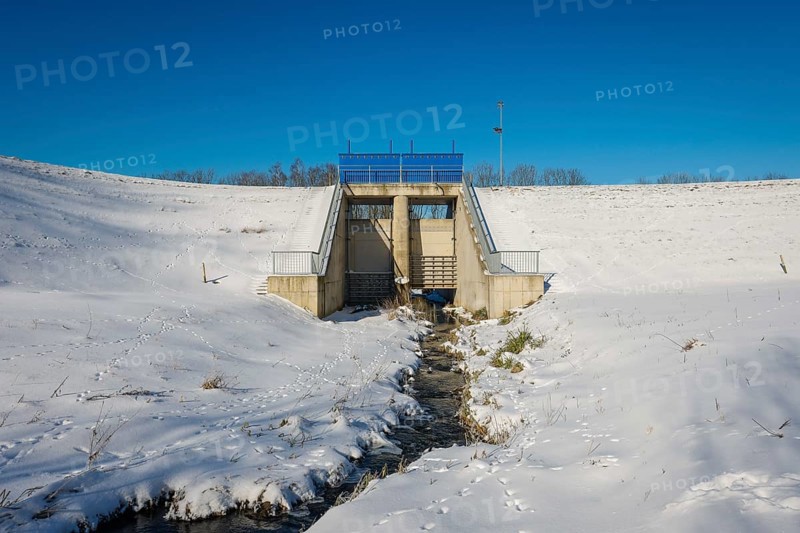 Bochum, North Rhine-Westphalia, Germany - Sunny winter landscape in the Ruhr area, ice and snow on the renaturalised Goldhammer Bach here at the HRB flood retention basin, the stream has been transformed into a near-natural body of water, the Goldhammer Bach flows via the Hüller Bach into the Emscher, is part of the Emscher river system and thus part of the Emscher conversion, was previously an open, above-ground wastewater canal, mixed water canal with surface water and wastewater, animal tracks in the snow, the gates are closed during floods