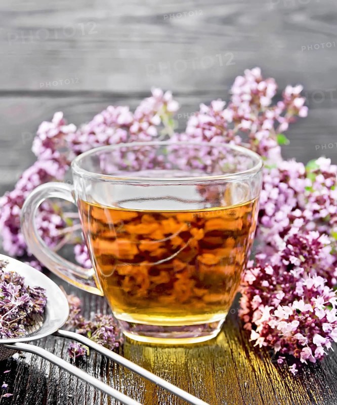 Oregano herbal tea in a glass cup, fresh flowers and metal strainer with dried marjoram flowers on wooden board