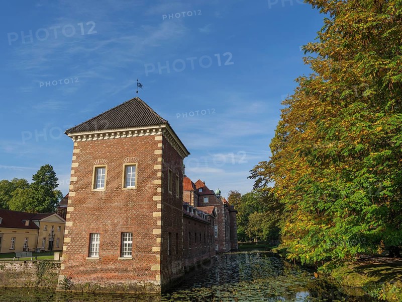 Historic brick building next to a river and autumn-coloured trees, velen, westphalia, germany