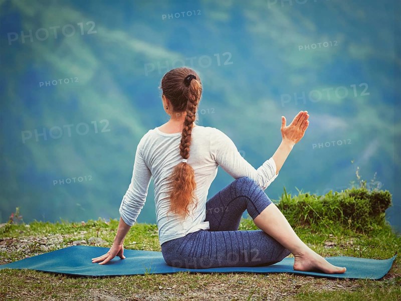 Hatha yoga outdoors, sporty fit woman doing yoga asana Parivrtta Marichyasana (or ardha matsyendrasana), seated spinal twist outdoors in mountains. Vintage retro effect filtered hipster style image