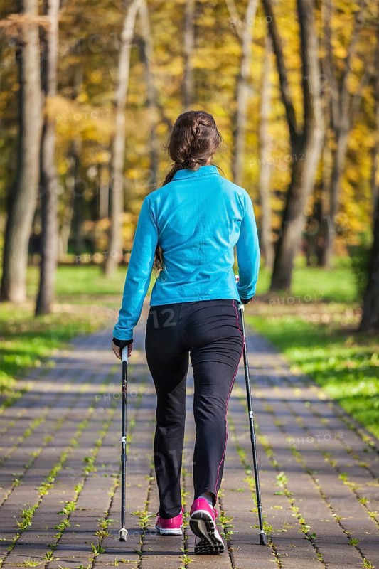 Nordic walking adventure and exercising concept, woman hiking withnordic walking poles in park