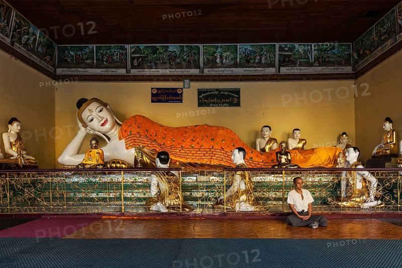 YANGON, MYANMAR, JANUARY 3, 2014: Man meditating near statue of Recumbent Buddha in Shwedagon Paya pagoda