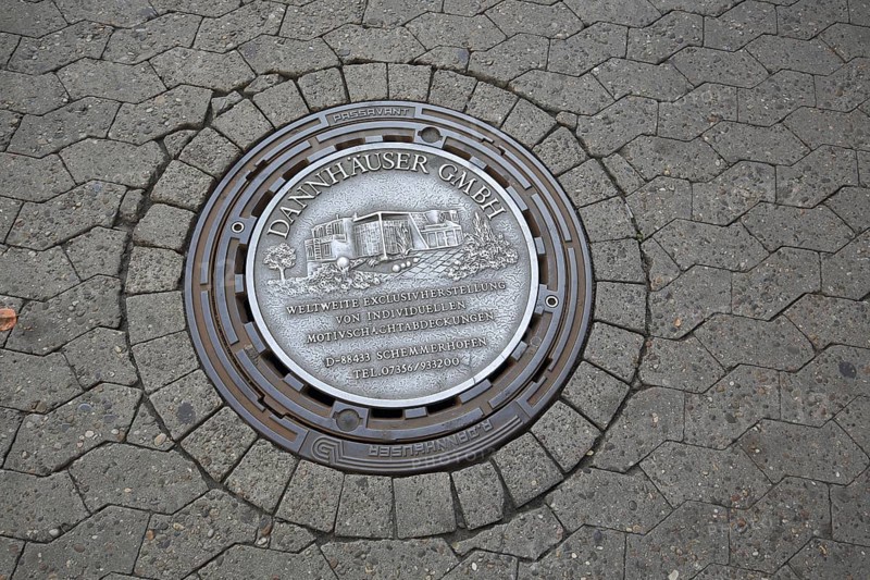 Manhole cover as advertising from the company Dannhäuser GmbH for individual production of motifs, casting, cast iron, foundry, metal, Bensheim, Bergstrasse, Hesse, Germany, Europe