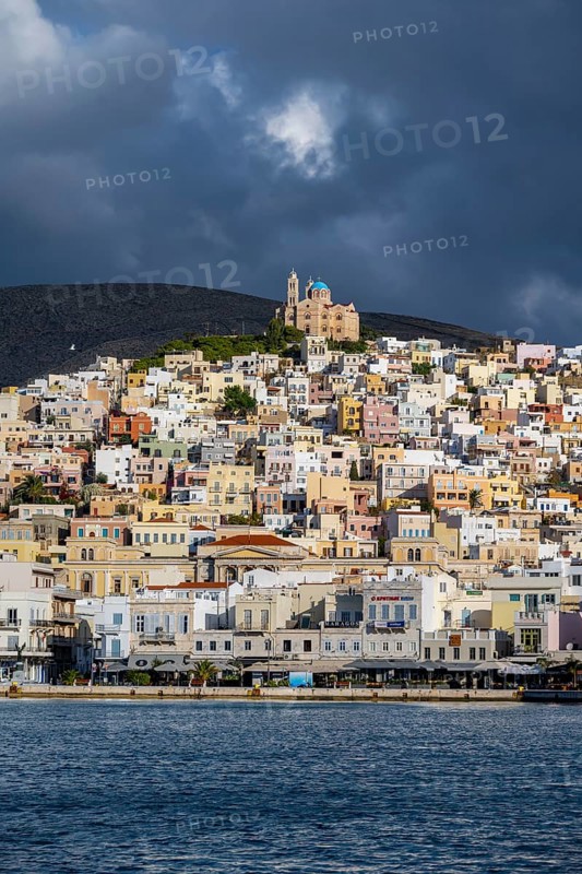 View of the town of Ermoupoli with pastel-coloured houses and the sea, on the hill Anastasi Church or Church of the Resurrection, dramatic cloudy sky, Ermoupoli, Syros, Cyclades, Greece, Europe