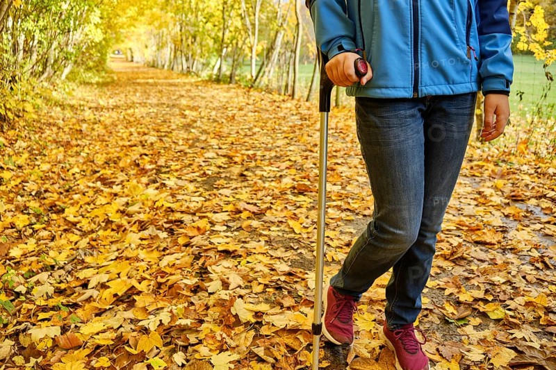 Young teenage girl walks with crutch through colourful autumn leaves