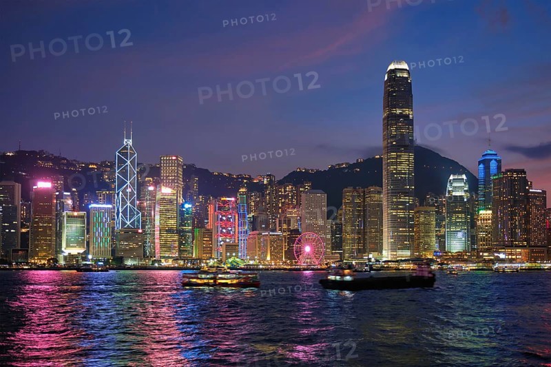 Hong Kong skyline cityscape downtown skyscrapers over Victoria Harbour in the evening illuminated with tourist boat ferries. Hong Kong, China, Asia