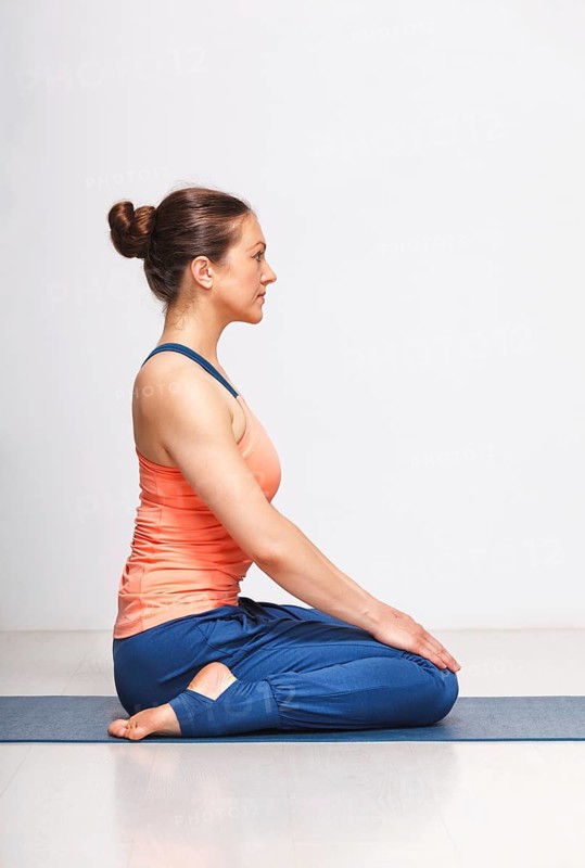 Woman in Hatha yoga asana Vajrasana, vajra pose or diamond pose on yoga mat on yoga mat in studio on grey bagckground