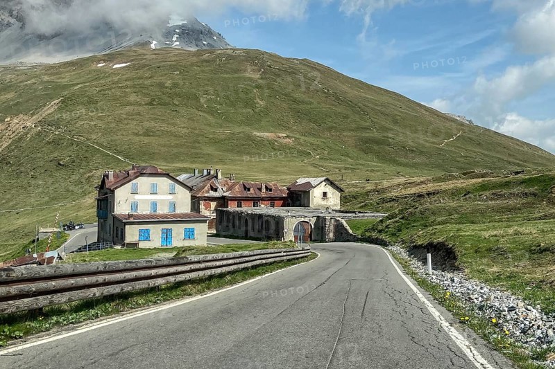 View on mountain road pass road alpine road above tree line southern descent from alpine pass pass Stelvio Stilfser Joch to Bormio, on the left old historical building hotel restaurant Albergo IV Cantoniera, on the right abandoned decaying houses, Bormio, Lombardy, Italy, Europe