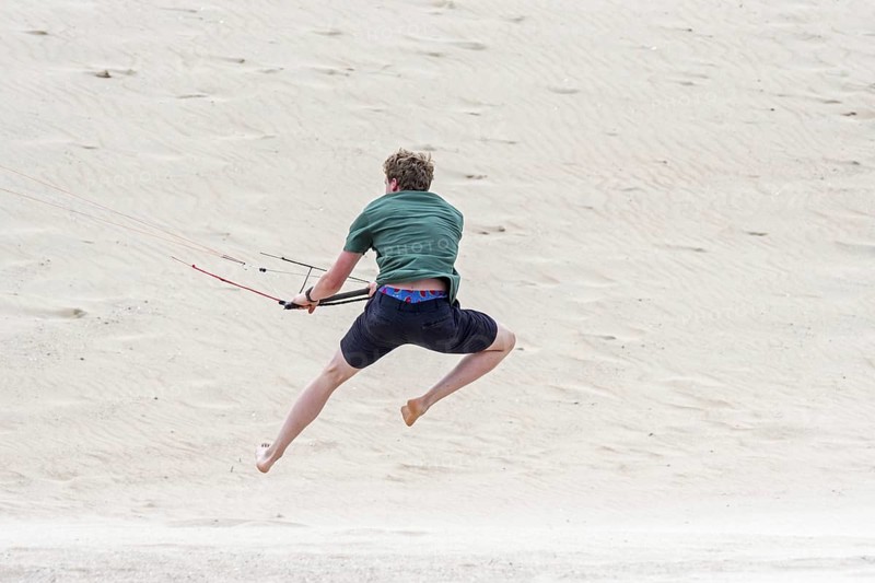 Young man handling 4 line control bar of a flying quad lines trainer parafoil, 4 line stunt kite on sandy beach in strong wind in summer