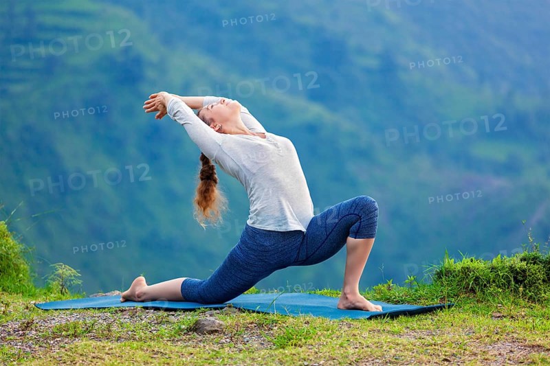 Yoga outdoors, sporty fit woman practices Hatha yoga asana Anjaneyasana, low crescent lunge pose posture outdoors in Himalayas mountains