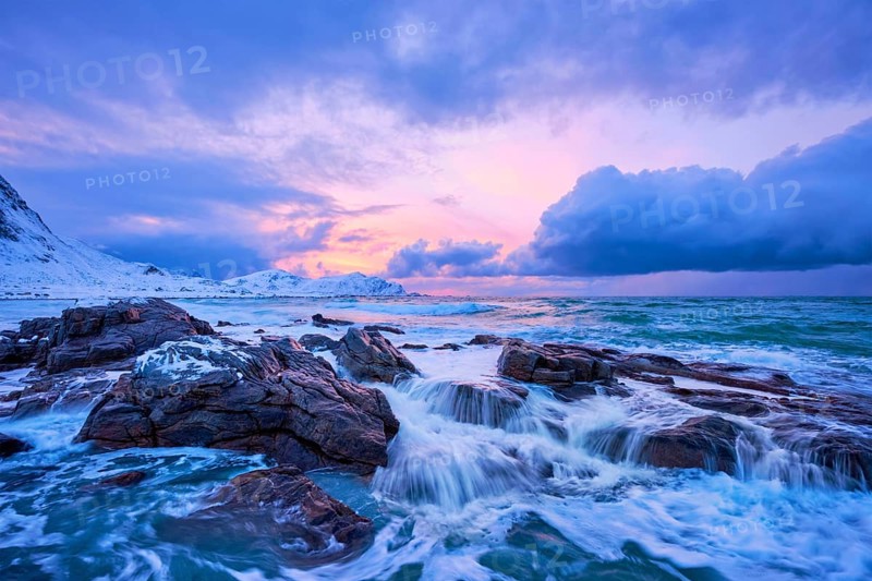 Waves of Norwegian sea on rocky coast in fjord on sunset with sun. Skagsanden beach, Lofoten islands, Norway, Europe