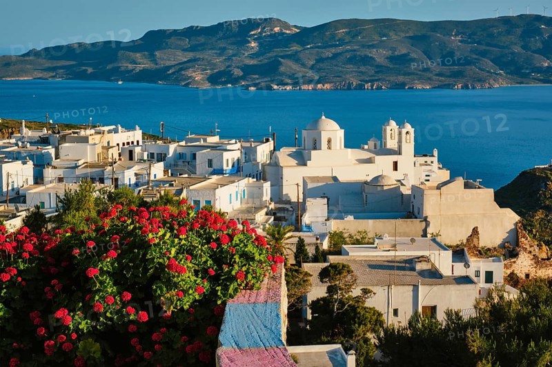 Picturesque scenic view of Greek town Plaka on Milos island over red geranium flowers. Plaka village, Milos island, Greece. Focus on flowers