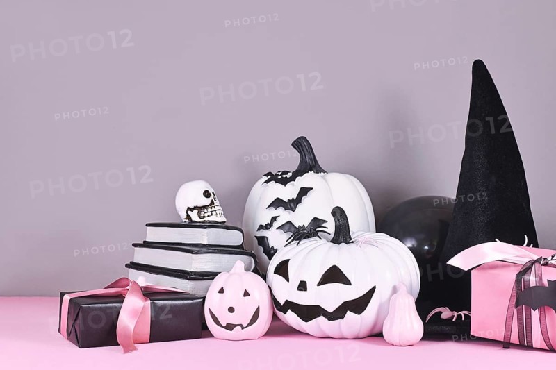 Pink and white Halloween decor with black and white pumpkins, witch hat and spell books on gray background
