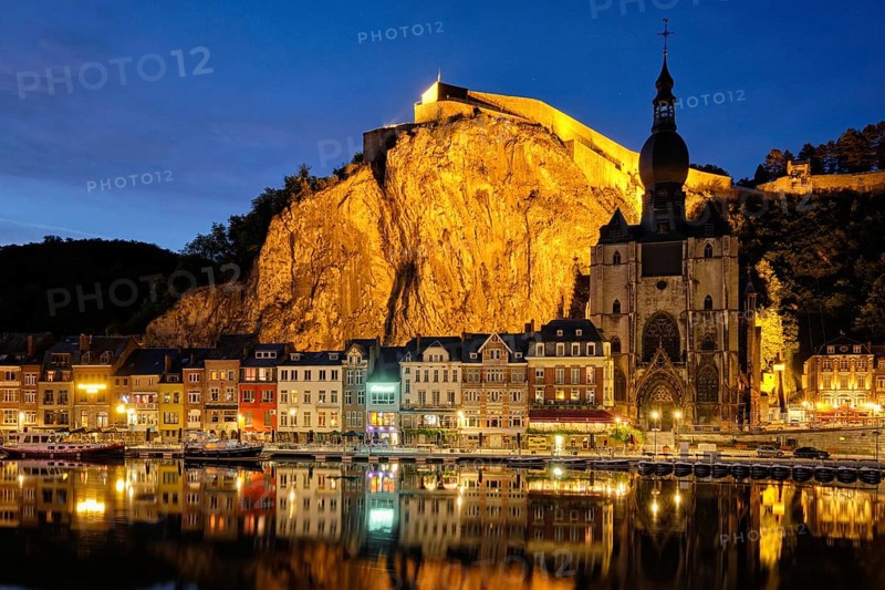Night view of Dinant town, Collegiate Church of Notre Dame de Dinant over River Meuse and Pont Charles de Gaulle bridge and Dinant Citadel illuminated in the evening. Dinant, Belgium, Europe