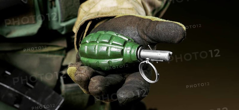 The soldier in full combat ammunition holds a grenade in his hand.