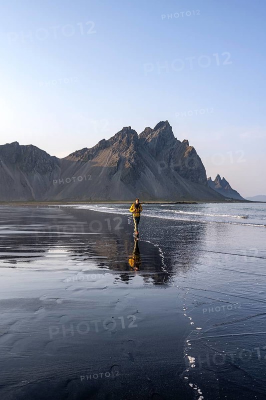 Tourist at black lava beach, sandy beach and sea, mountains Klifatindur reflected in the water, Eystrahorn and Kambhorn, headland Stokksnes, mountain range Klifatindur, Austurland, East Iceland, Iceland, Europe