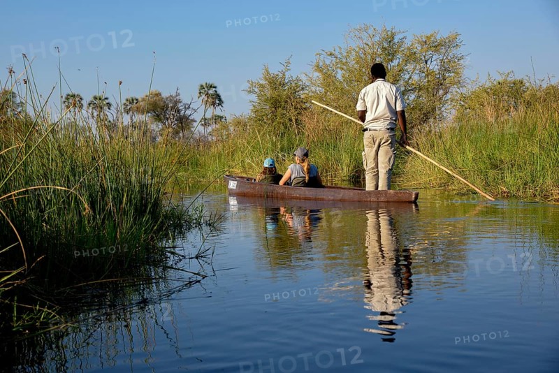 Tourists in a mokoro or dugout boat on safari in swamp area, Gomoti Plains Camp, Gomoti Concession Area, Okavango Delta, Botswana, Africa
