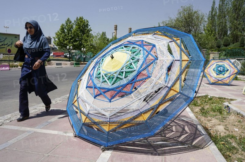 A woman walks past large umbrellas lying on the pavement in Tehran. The city of Tehran is changing the image of the city through art objects in public spaces, 17.05.2016