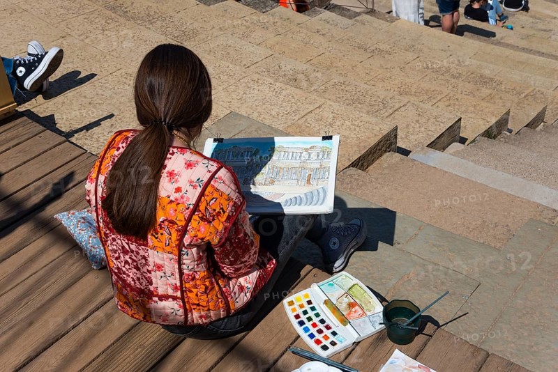 Woman painting with watercolours on the steps of a Roman theatre, surrounded by painting tools and brushes, Teatro Romano de Mérida, Roman theatre of Merida, Merida, Badajoz, Extremadura, Spain, UNESCO World Heritage Site, Europe
