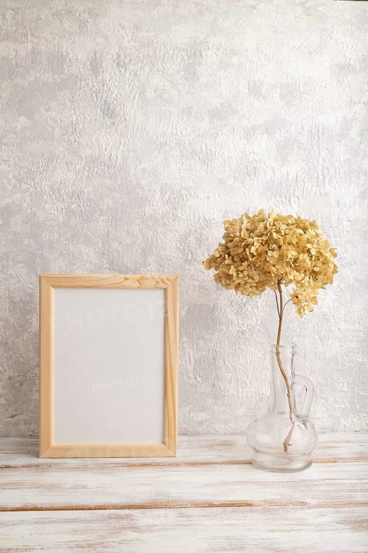 White wooden frame mockup with dried hydrangea in glass on gray concrete background. Blank, vertical orientation, still life, copy space