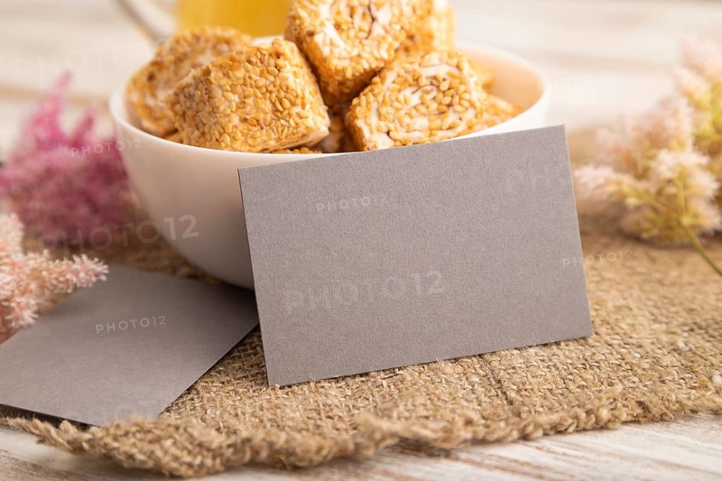 Gray business card with traditional turkish delight (rahat lokum) in white ceramic bowl on a white wooden background. side view, close up