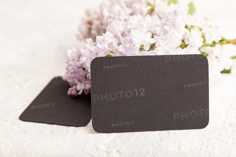 Black business card with lilac flowers on gray concrete background. side view, copy space, mockup, template, spring, summer minimalism concept