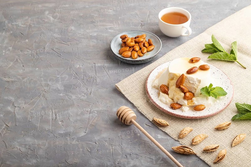 Ricotta cheese with honey and almonds on gray concrete background and linen textile. side view, copy space