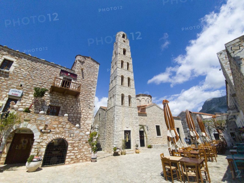 Old stone tower in a square with open parasols and blue sky, Taxiarchis Church, Old Town, Areopoli, Areopolis, Tsimova, Itylo, Anatoliki Mani, Mani, Laconia, Peloponnese, Greece, Europe